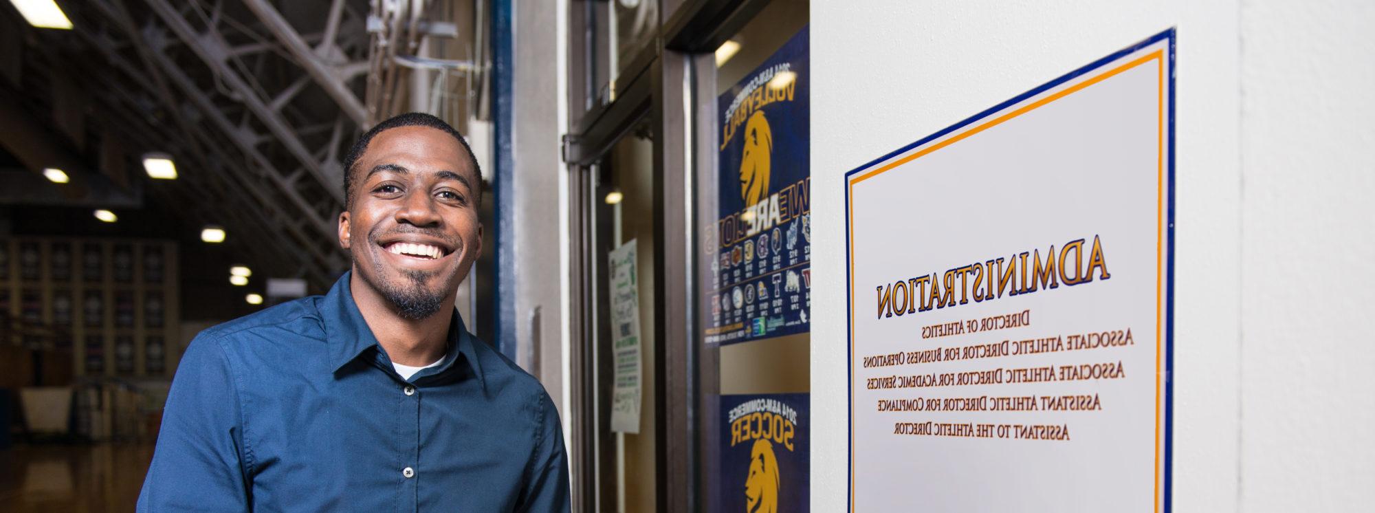 Athletic Administration Student smiling at the camera by the door of the TAMUC Athletics administration department. 