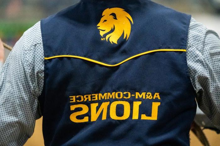A person wearing a blue vest that reads "A&M-Commerce Lions" in gold stitching.